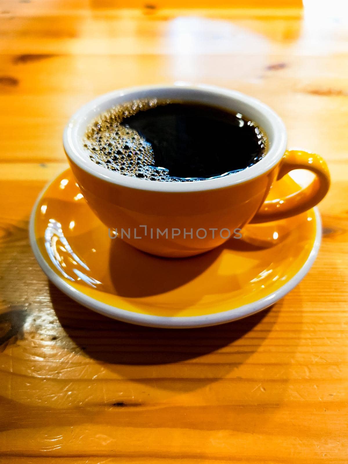 Yellow cup of black overflow coffee in small cafe by Wierzchu