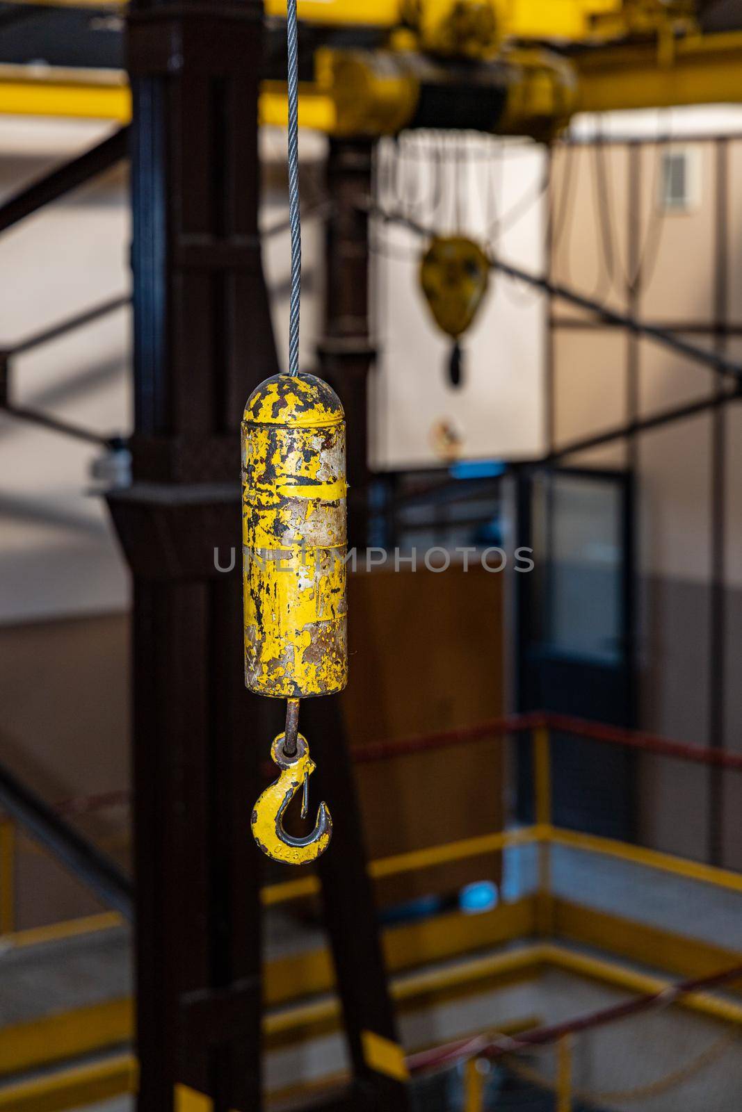Yellow hook hanged on steel rope inside big factory hall by Wierzchu