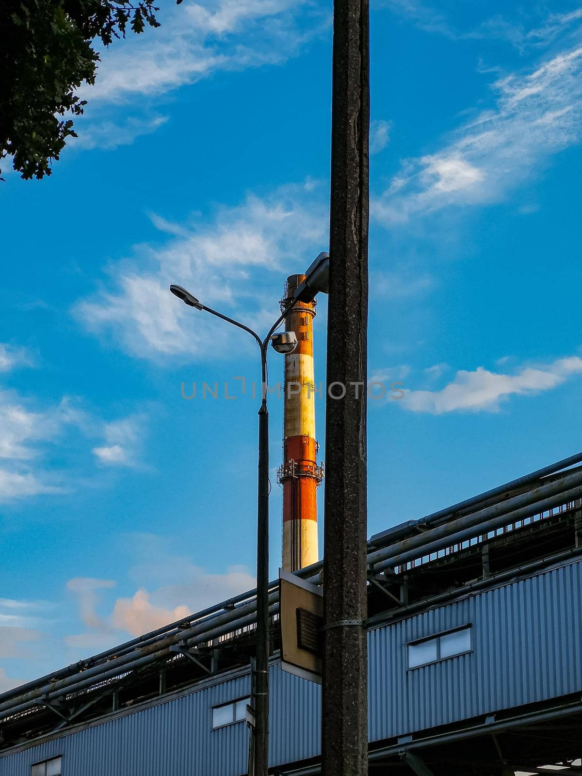 High white and red chimney between high pole and city lantern at sunny day by Wierzchu