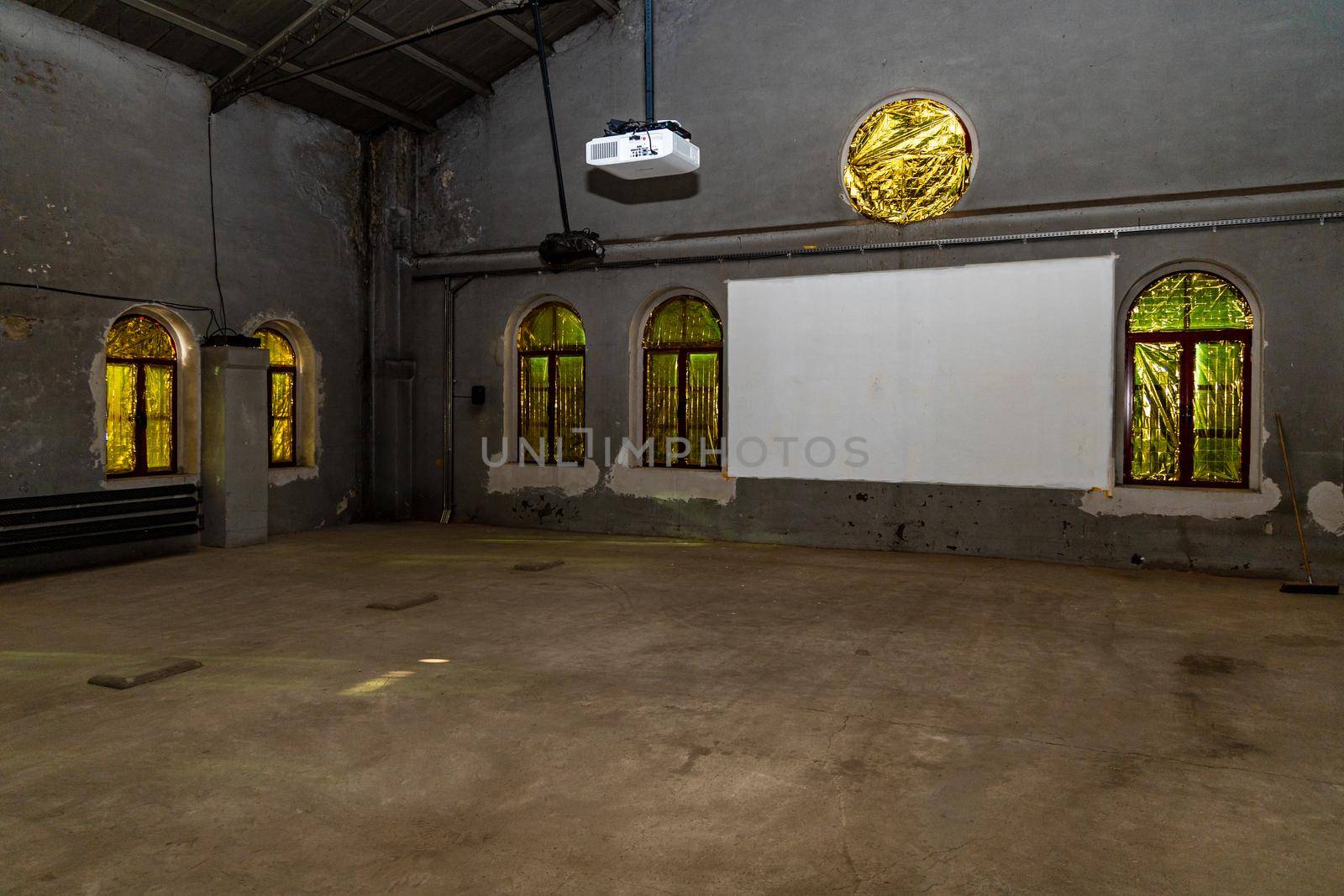 Dark big hall full of windows with yellow and green foil and projector with piece of white wall