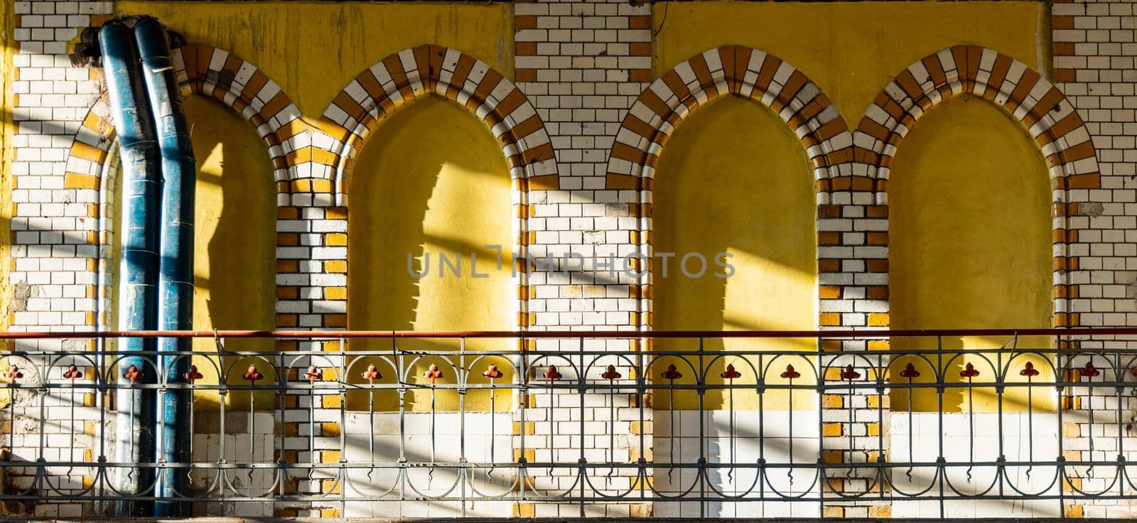 Arcs made of red and white tiles on yellow wall at balcony inside pumping station