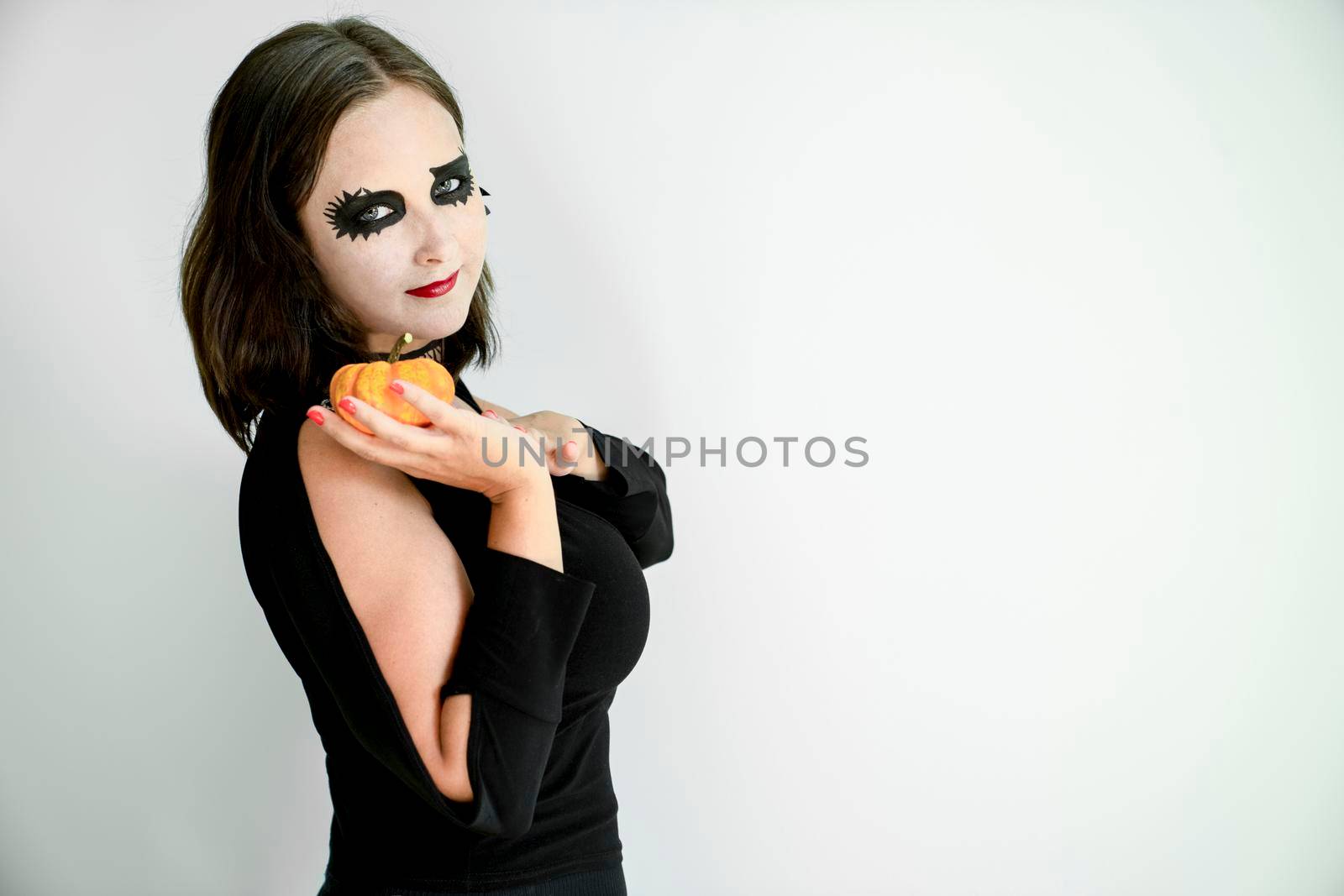 Girl with Halloween makeup on face holds pumpkin in hand on gray background. Copy space.