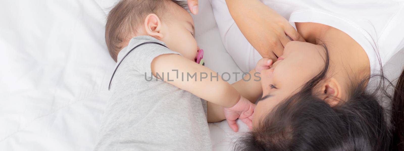 Young asian mother touch head of little baby girl with tender on bed in the bedroom, mom love newborn and care, woman with expression with child together, parent and daughter, family concept.