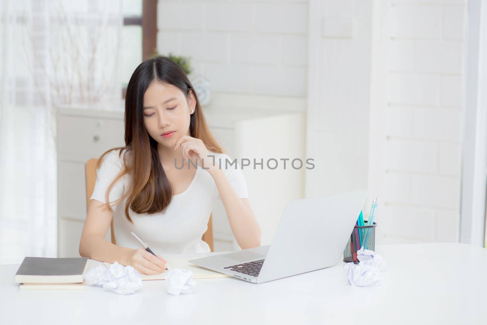 Young asian woman working with laptop computer think idea project and paper crumpled having problem on table at home, girl using notebook with frustrated and trouble, business and freelance concept. by nnudoo
