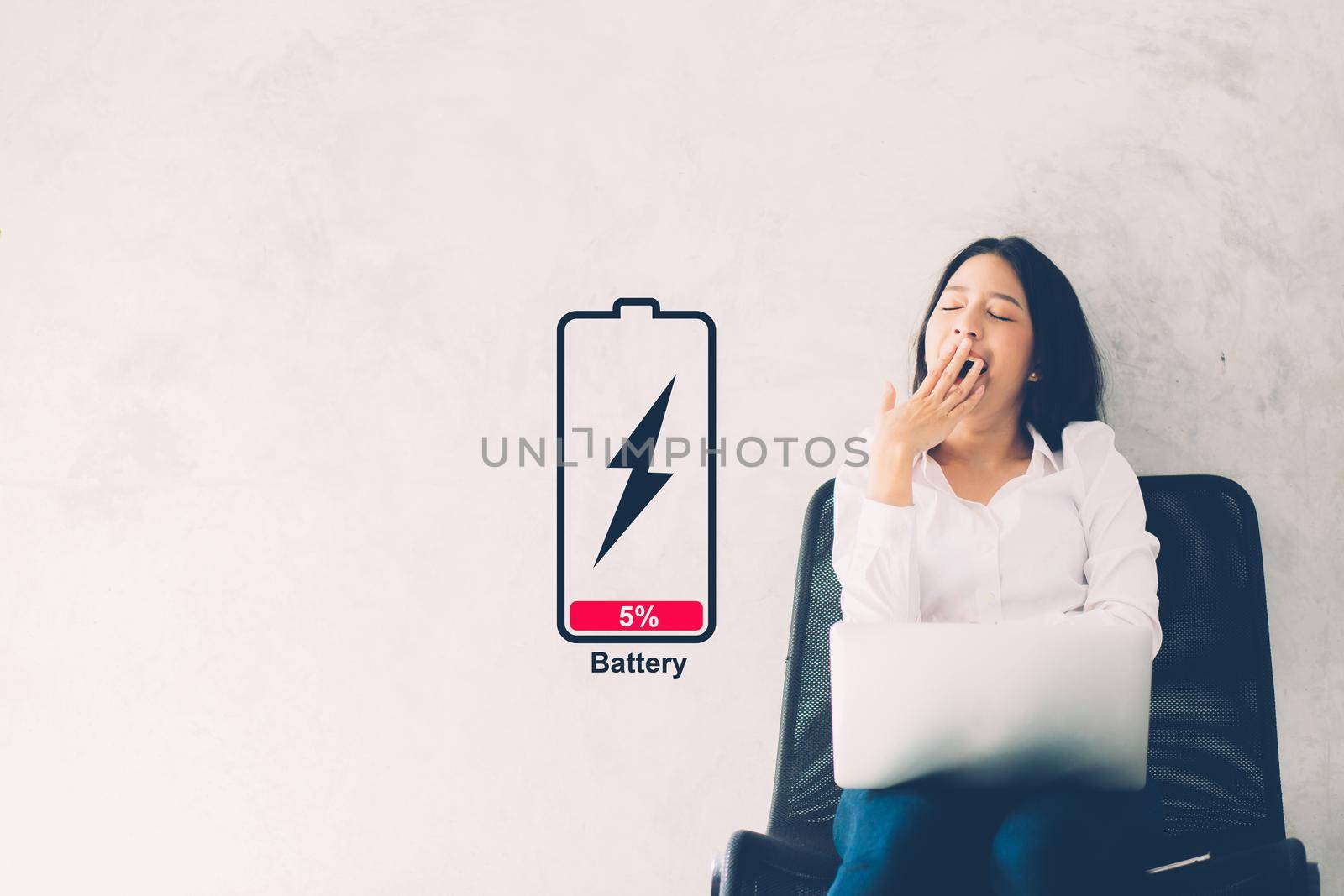 Young asian woman yawn at her work place with laptop computer on cement background, girl working with yawn and burnout with symbol battery low, stress and tired, copy space, business concepts. by nnudoo