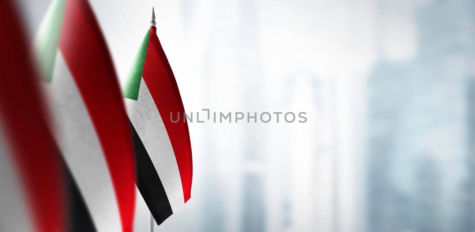 Small flags of Sudan on a blurry background of the city by butenkow