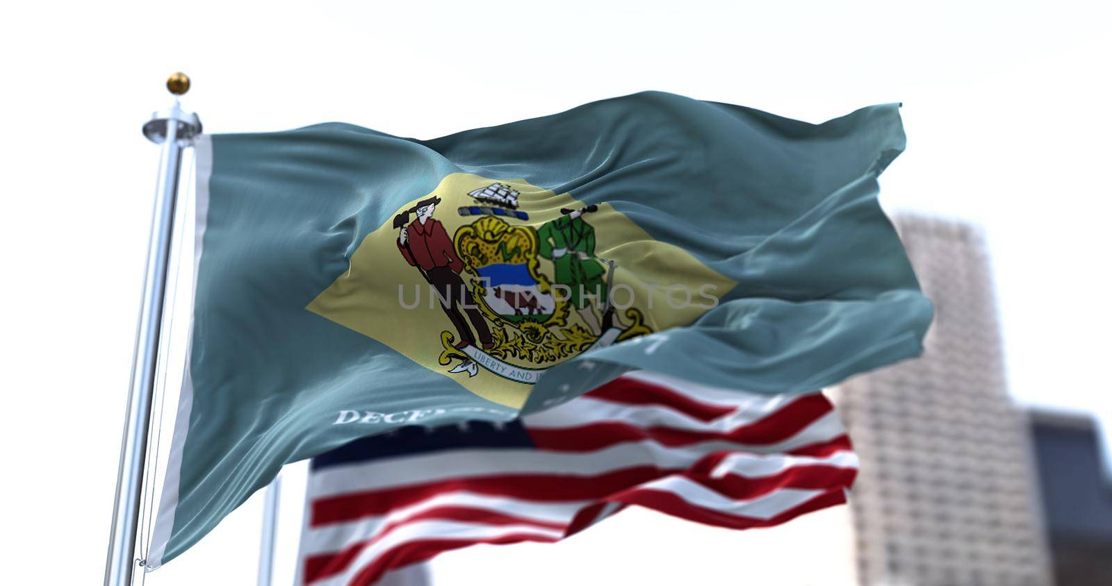 the flag of the US state of Delaware waving in the wind with the American stars and stripes flag blurred in the background by rarrarorro