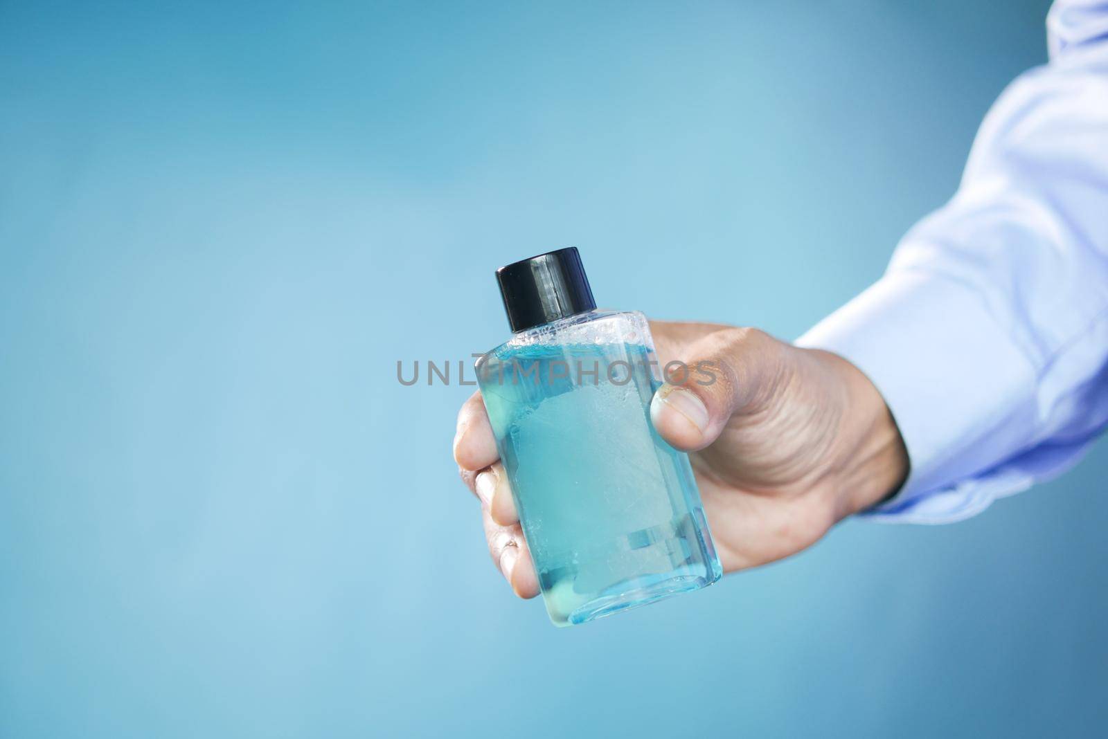 hand hold a mouthwash liquid container against blue background by towfiq007