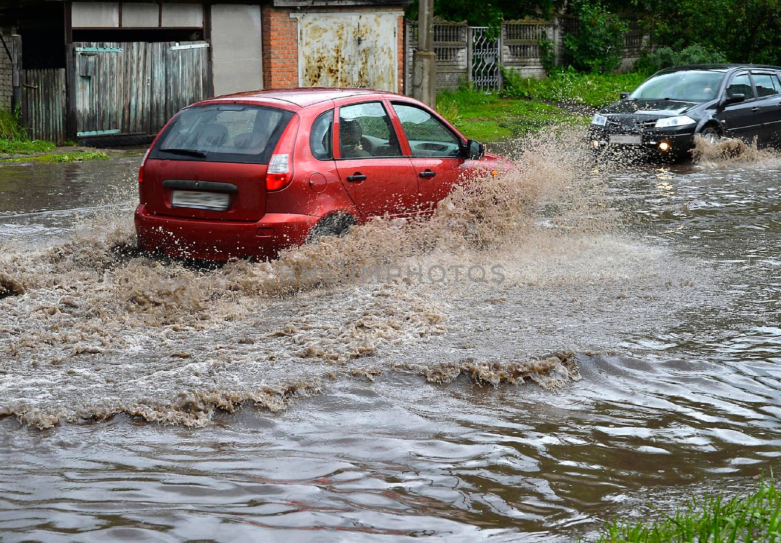Cars drive in pouring rain on a flood-flooded road.