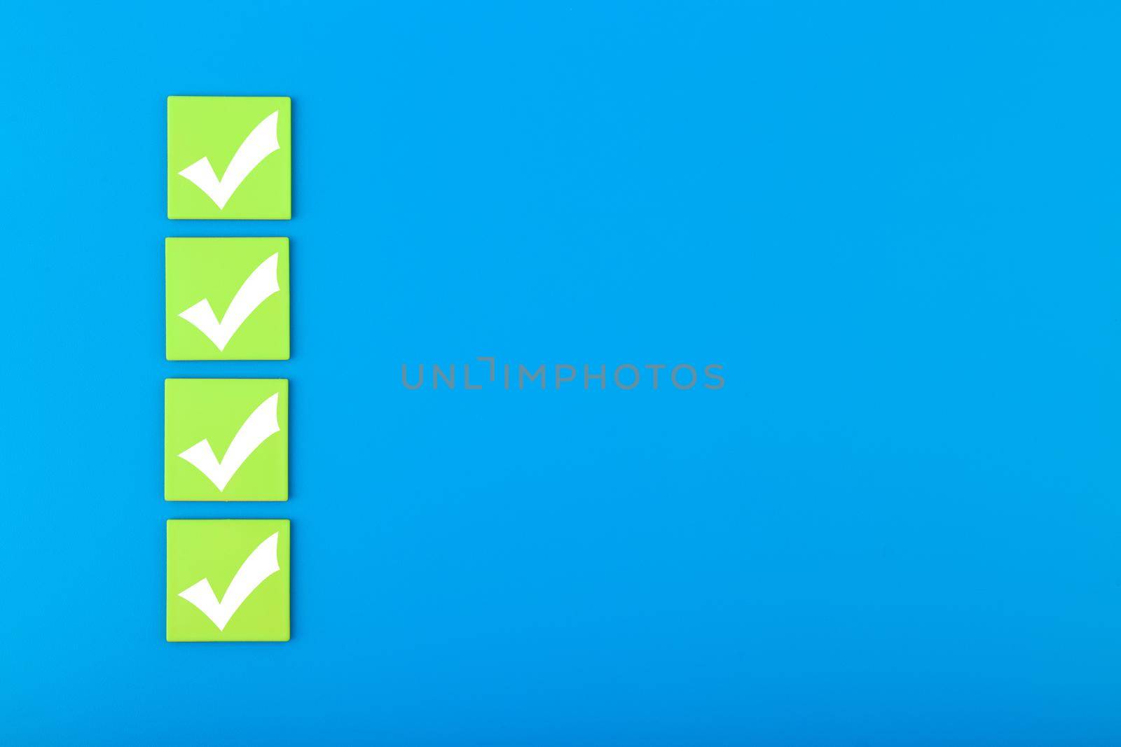 Four checkmarks on green tablets in a row on blue background with copy space. Concept of questionary, checklist, to do list, planning, business or verification. Modern minimal composition 