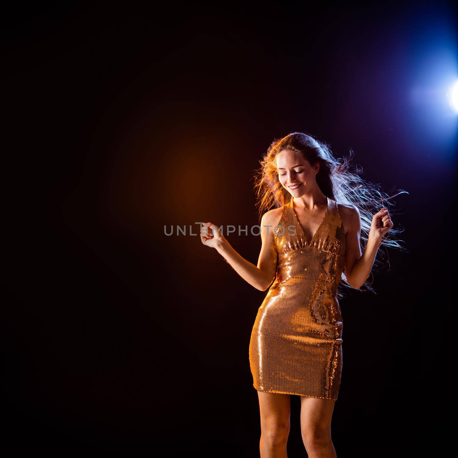 Beautiful girl in Golden dress dancing on black background, color lights