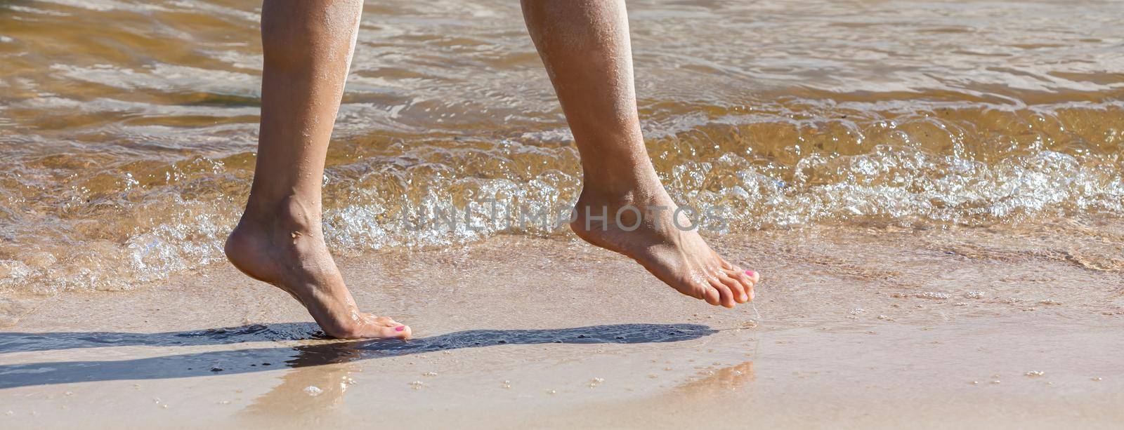 Young woman walking along the sandy beach. Female legs in the sand on the seaside