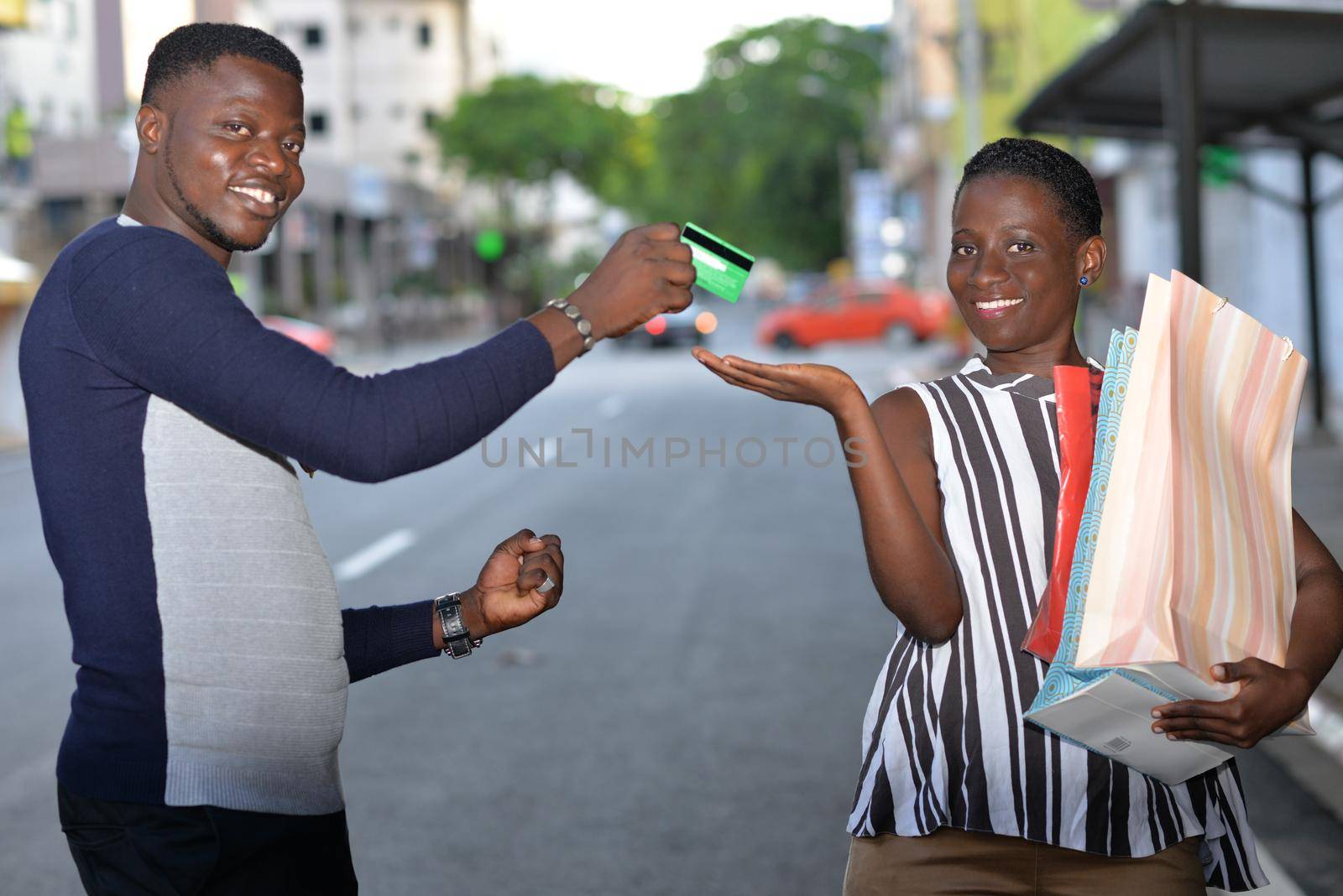 young man standing in polo gives credit card to his girlfriend smiling on camera.