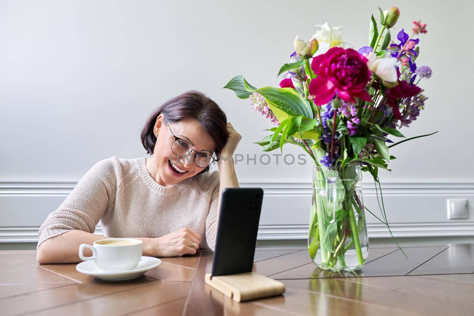 Smiling middle aged woman talking looking at smartphone screen, online virtual meeting conversation, female blogger vlogger recording blog vlog communicating with followers