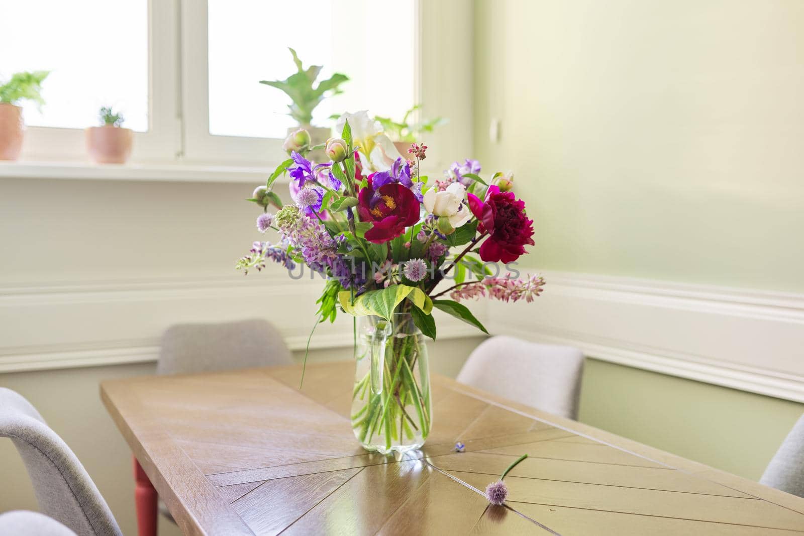 Bouquet of bright flowers on the table in jug. Flowers and buds of peonies irises lupine, season spring summer, home natural decor, holiday, gift concept