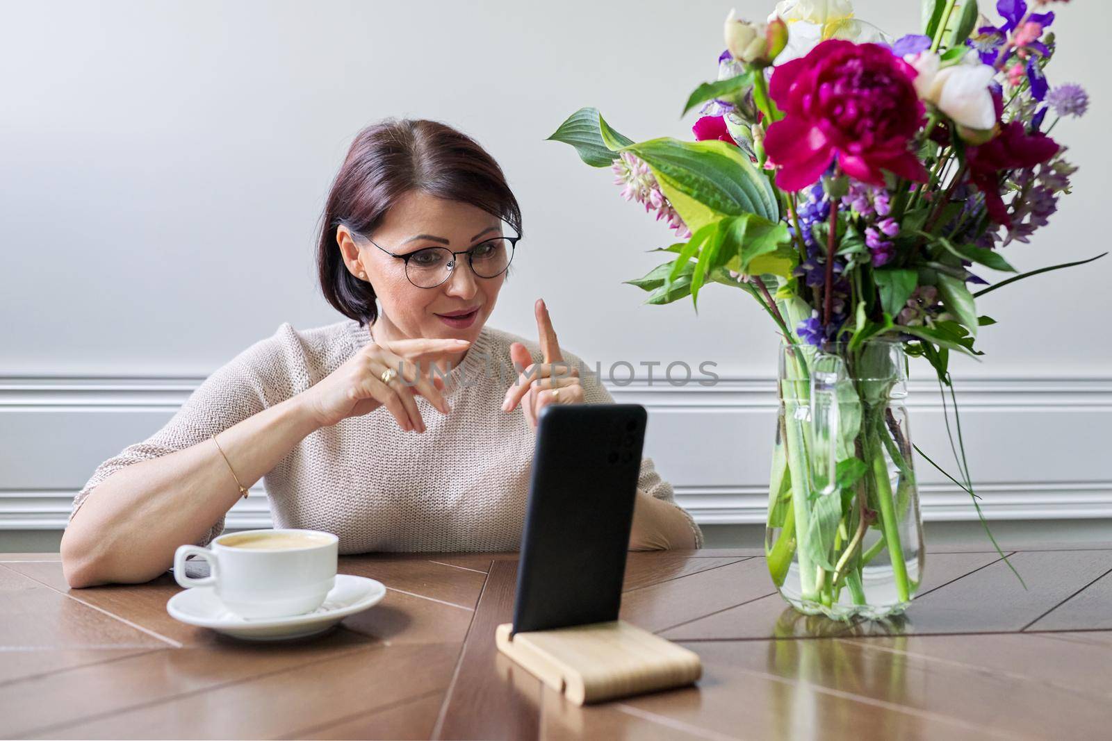 Smiling middle aged woman talking looking at smartphone screen, online virtual meeting conversation, female blogger vlogger recording blog vlog communicating with followers