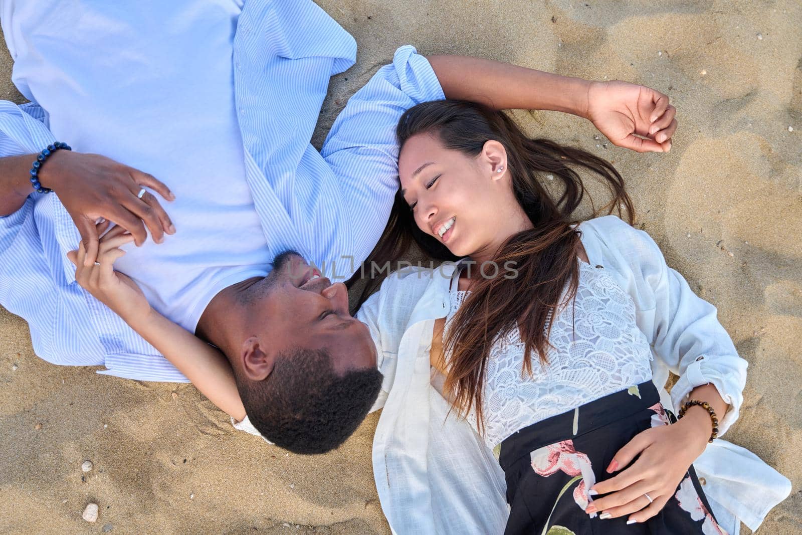 Top view of young interracial couple in love. African american man and asian woman lying together on the sand. Love, relationship, lifestyle, dating, multiethnic family, happiness concept
