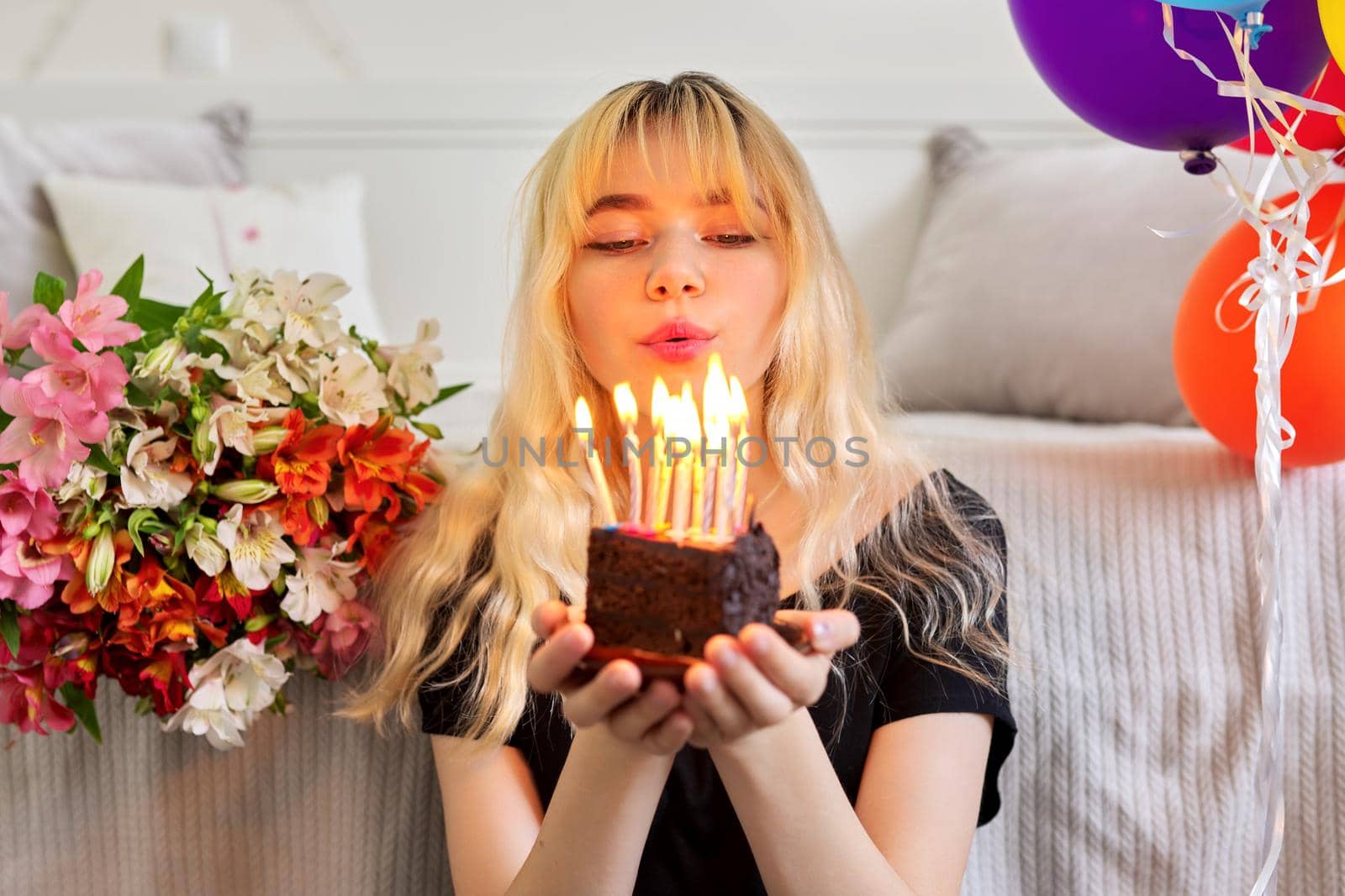 Birthday of female teenager, girl with birthday small cake with burning candles, room, bouquet of flowers, colored balloons background. Holiday, teens, age, celebration concept