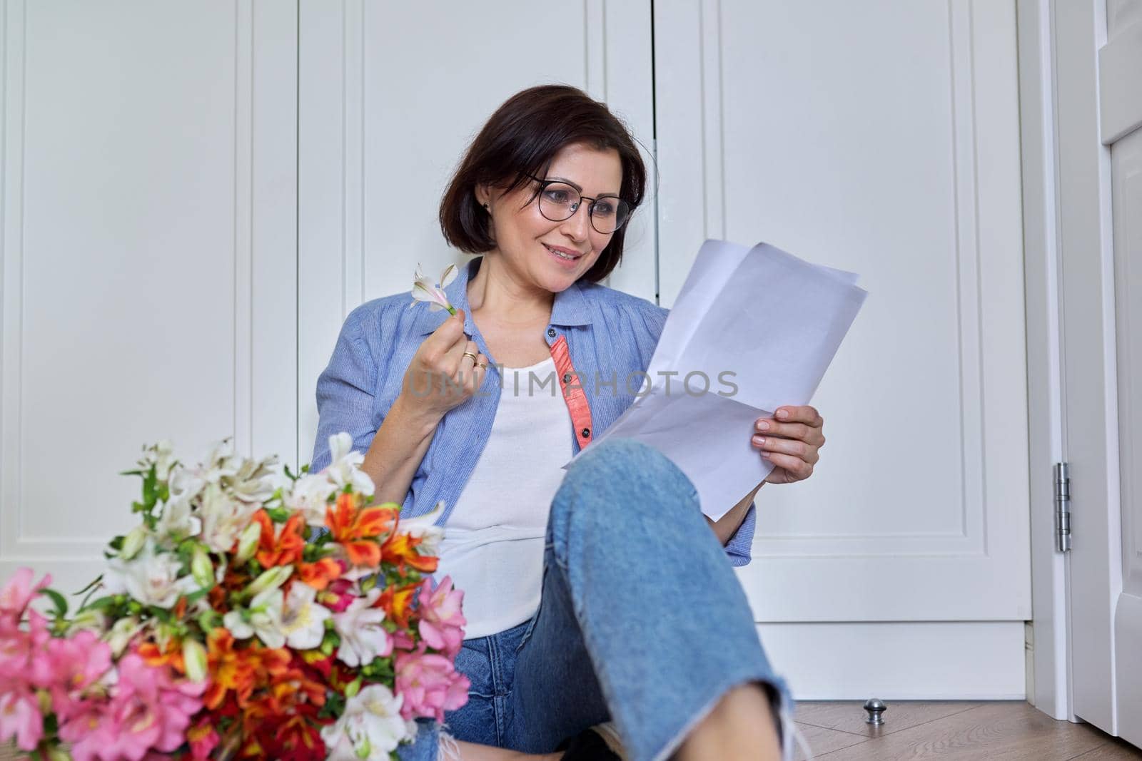 Middle-aged smiling female with a bouquet of flowers reading paper by VH-studio