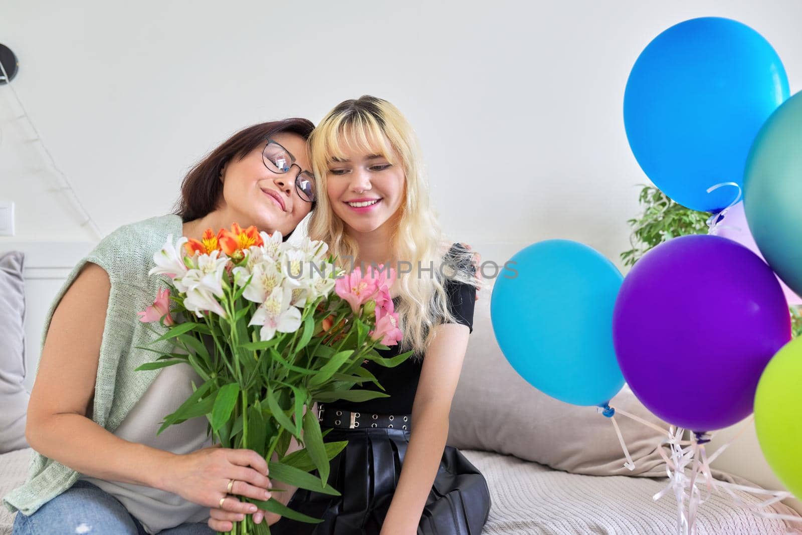 Portrait of happy smiling mom and teenage daughter, birthday celebration, women with bouquet of flowers colored balloons. Holiday, birthday, parent teenager relationship concept