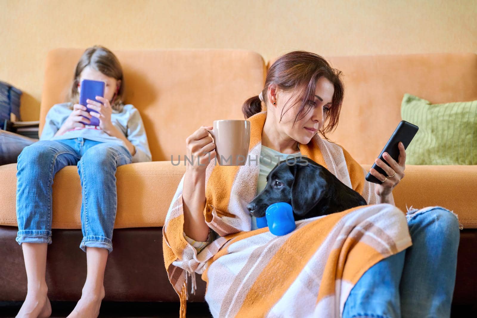 Family, home, lifestyle, pets, technology, communication, relaxation, e-learning, online reading, leisure. Mom, daughter child and dog sitting at home on couch looking at smartphone screen