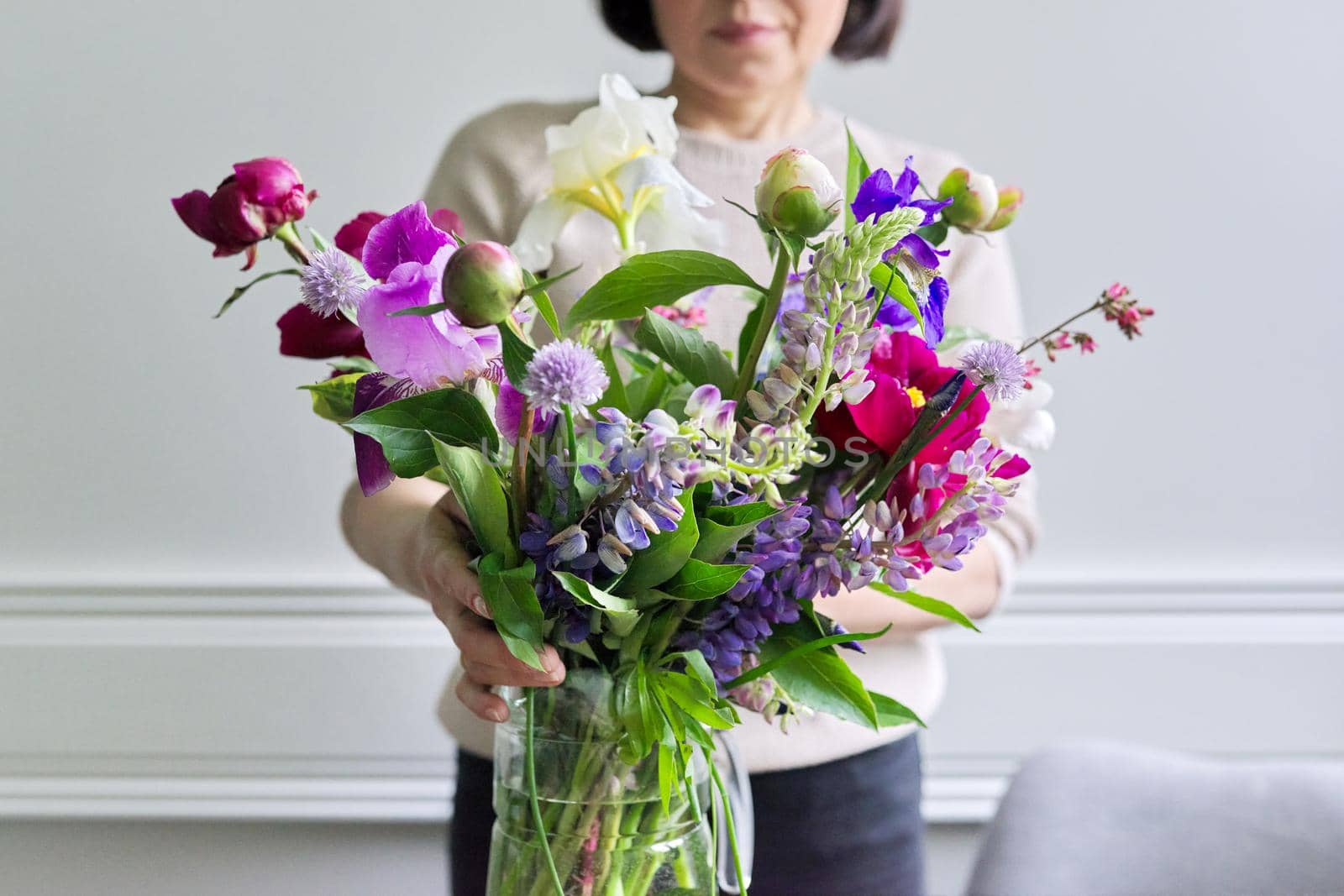 Bouquet of bright flowers of peonies irises lupins in the hands of woman close-up by VH-studio