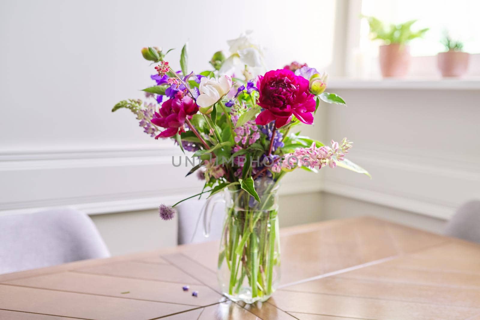 Bouquet of bright flowers on the table in jug. Flowers and buds of peonies irises lupine, season spring summer, home natural decor, holiday, gift concept