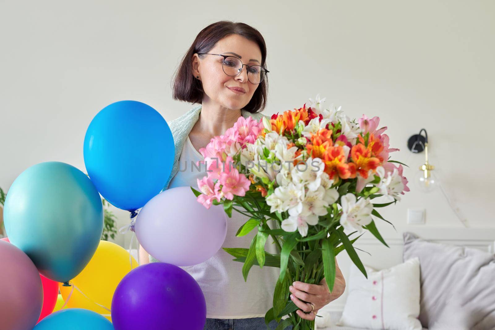 Birthday, 45 years old, happy middle-aged female with bouquet of flowers and balloons at home in the room. Mature age, celebration, anniversary, people concept