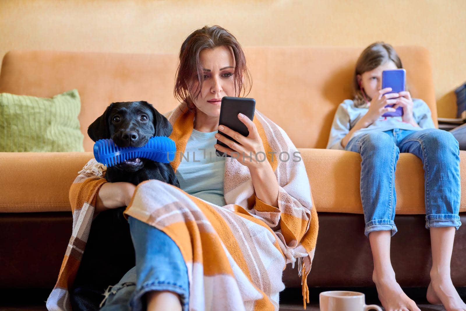 Family, home, lifestyle, pets, technology, communication, relaxation, e-learning, online reading, leisure. Mom, daughter child and dog sitting at home on couch looking at smartphone screen