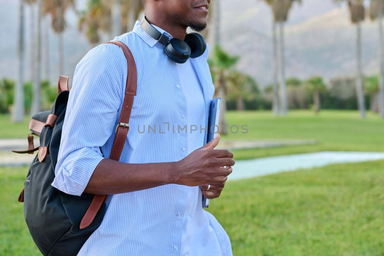 Outdoor portrait of young man with laptop headphones and backpack by VH-studio