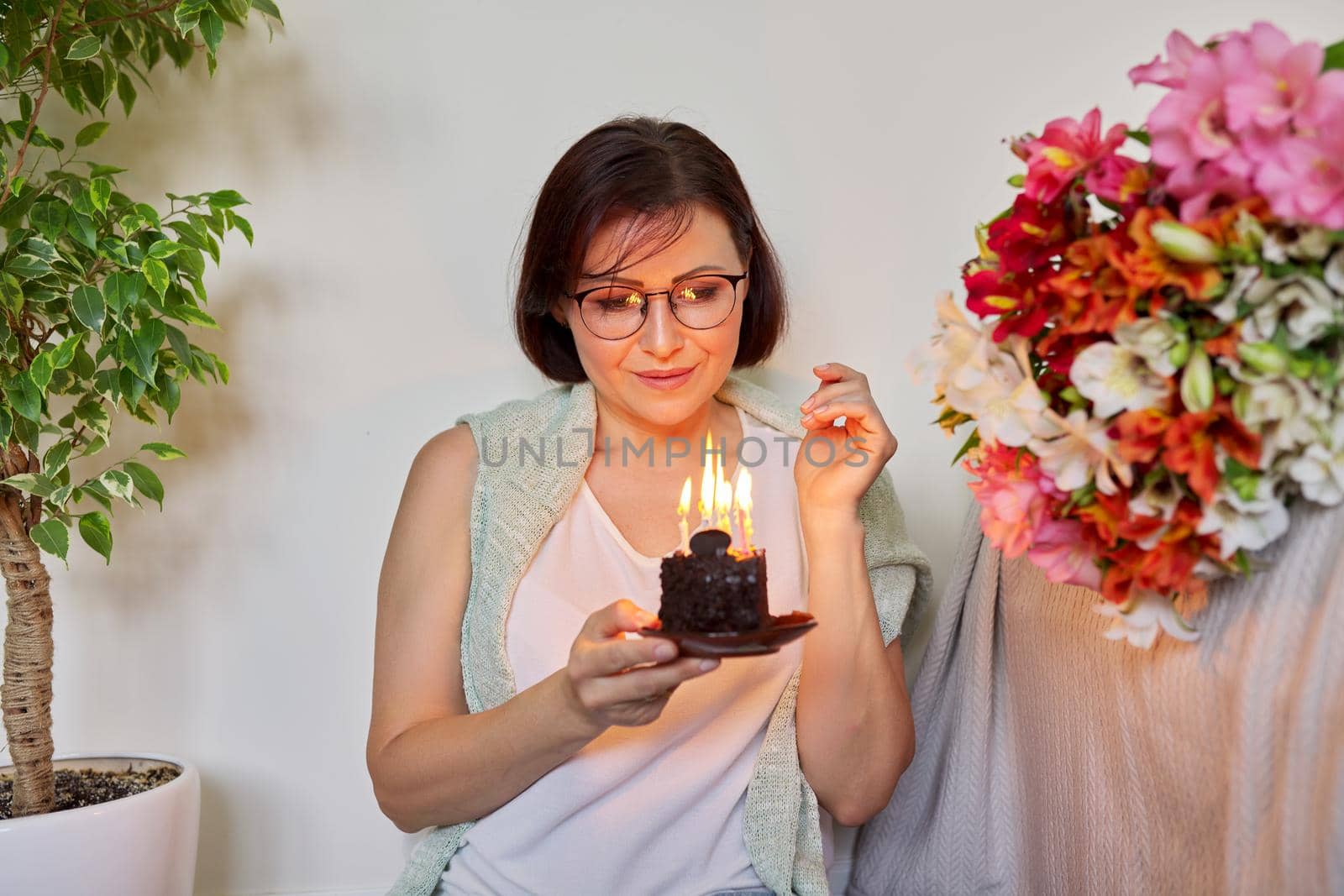 Mature woman with small birthday cake with burning candles by VH-studio