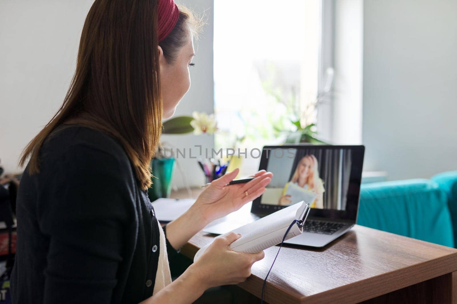 Woman teacher teaching at home online, distance learning. Female sitting at home at table with laptop on virtual meeting with teenage student, video call. E-learning modern technologies in education