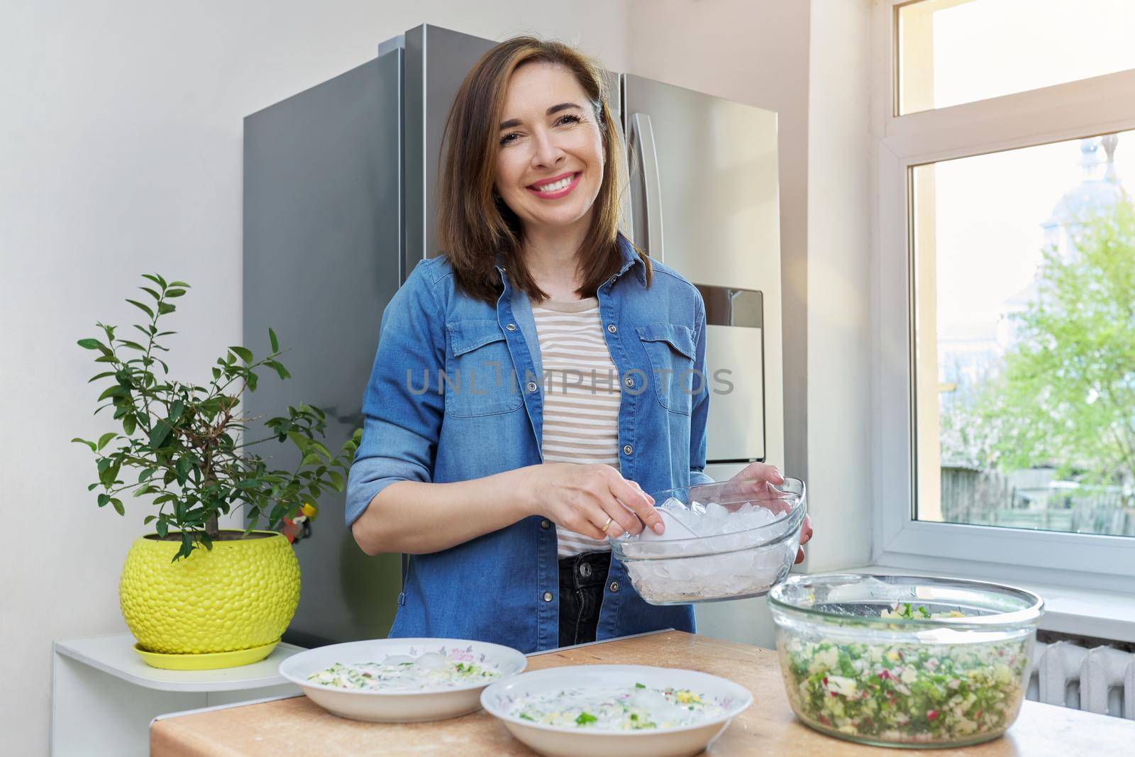 Smiling woman in kitchen near refrigerator with ice for cooling food by VH-studio