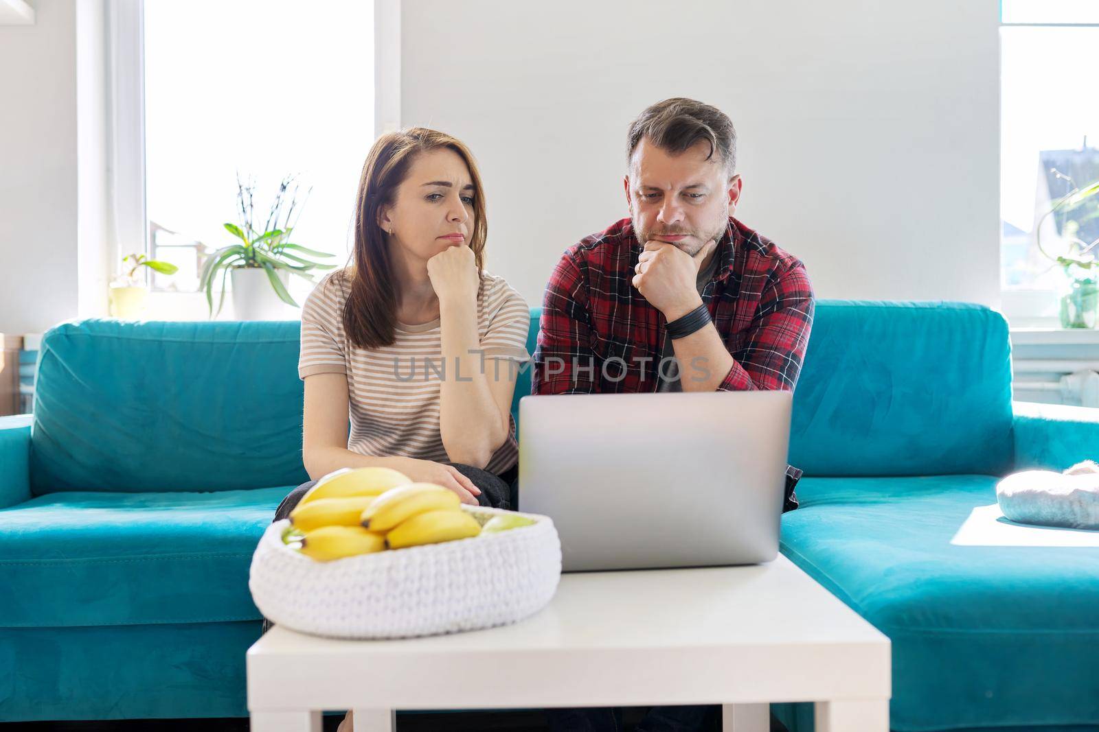 Serious middle-aged couple husband and wife with laptop sitting at home on couch by VH-studio