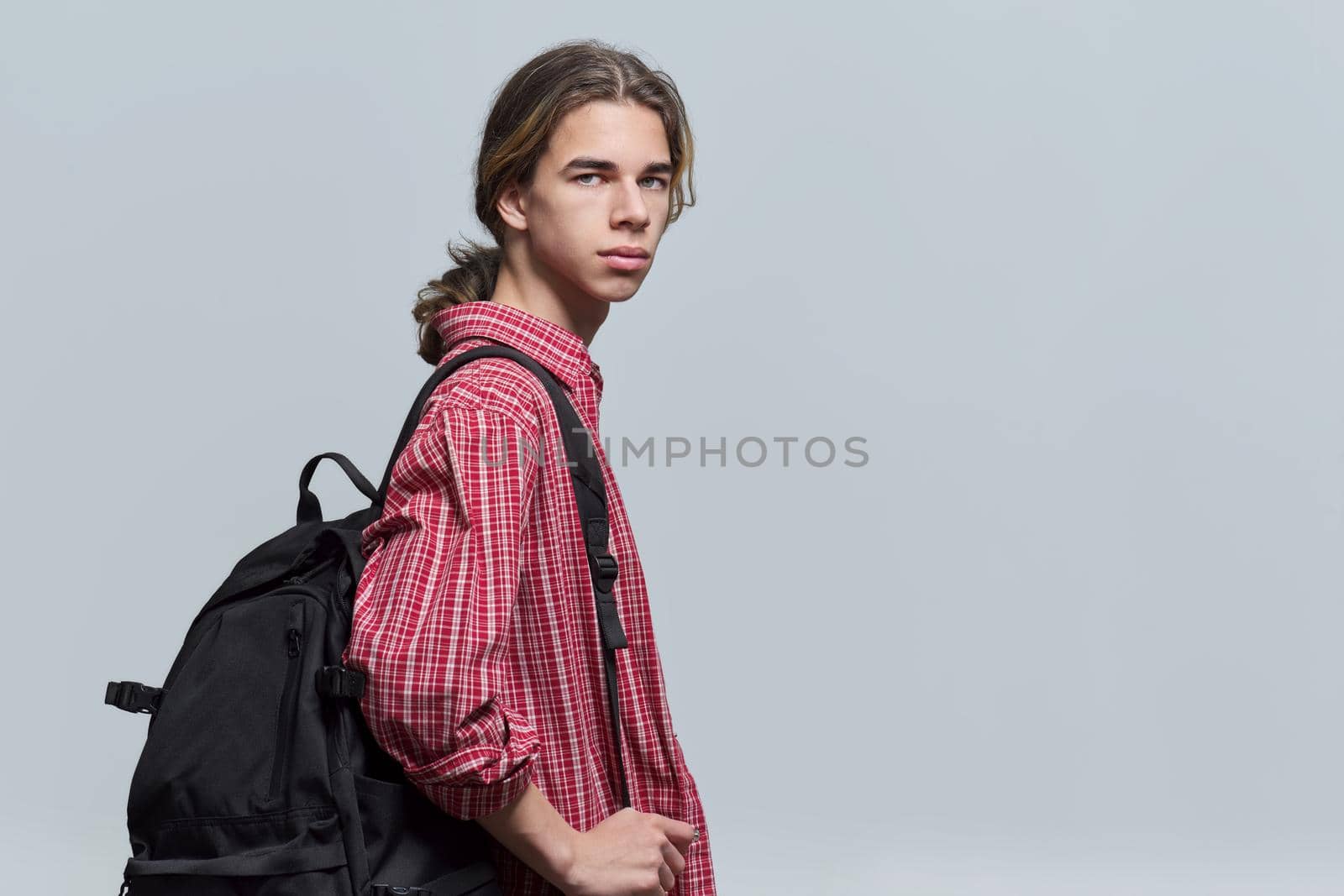 Guy student teenager with backpack looking at camera on light background, copy space. Portrait of handsome hipster teen male