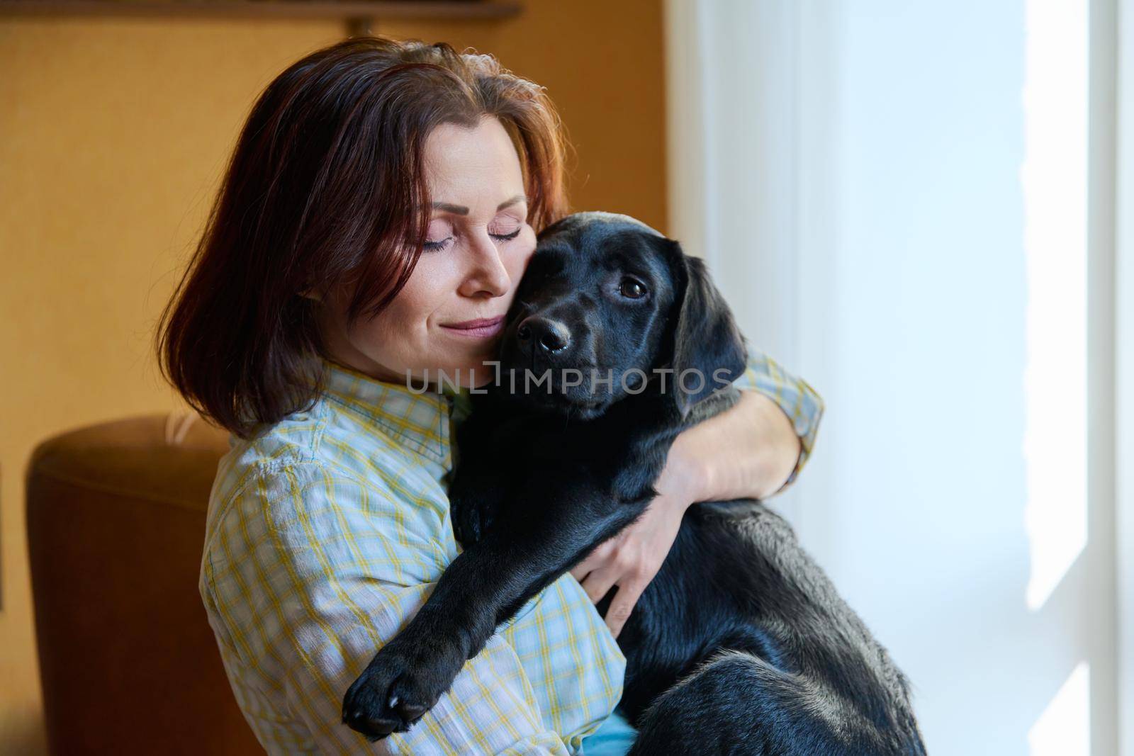 Portrait of middle aged woman and black labrador puppy dog by VH-studio