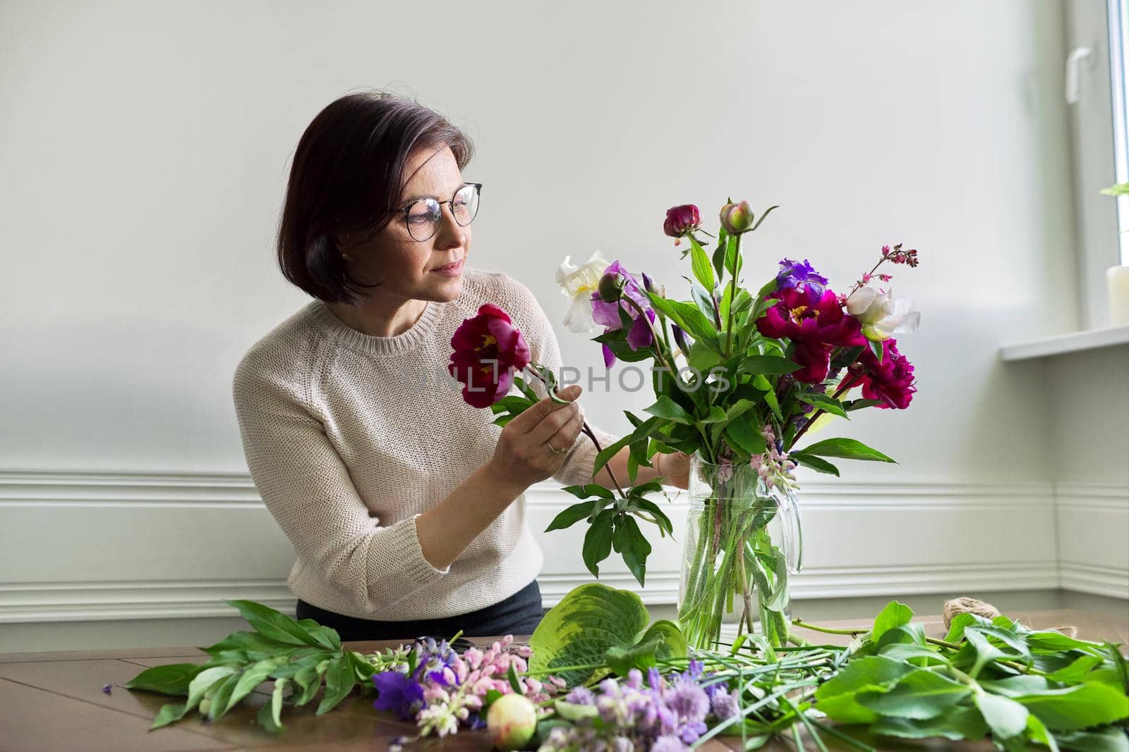 Mature woman at home with spring flowers by VH-studio