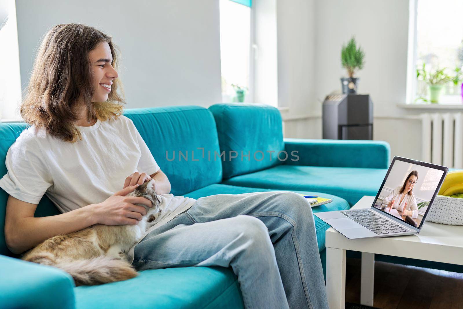 Guy talking online with teacher, psychologist, social worker. Teenager sitting at home with pet cat, using video call on laptop, virtual meeting with counselor. Technology, adolescence, mental health