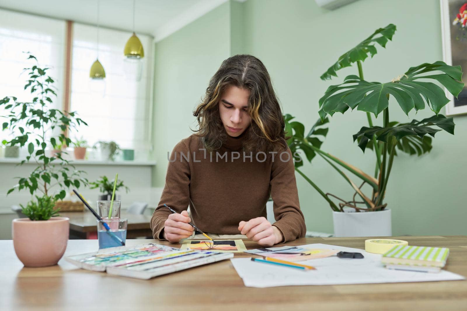 Talented creative guy teenager painting with watercolors, sitting at the table at home. Creativity, youth, teenagers, lifestyle concept