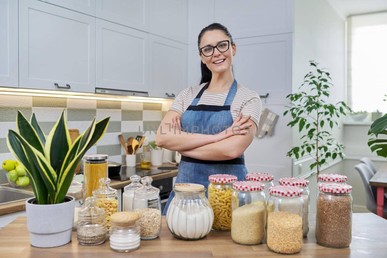 Portrait of smiling woman housewife in an apron in kitchen by VH-studio