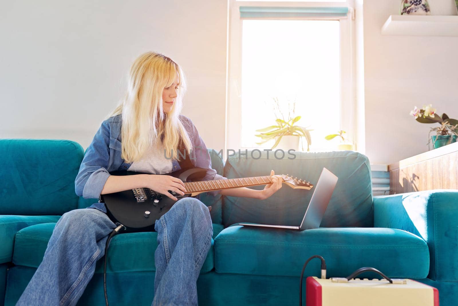 Hipster teenager girl playing electric guitar looking at laptop. Online learning music, songs, self-education, teen blogger musician recording video blog vlog, teaching, taking musical online courses