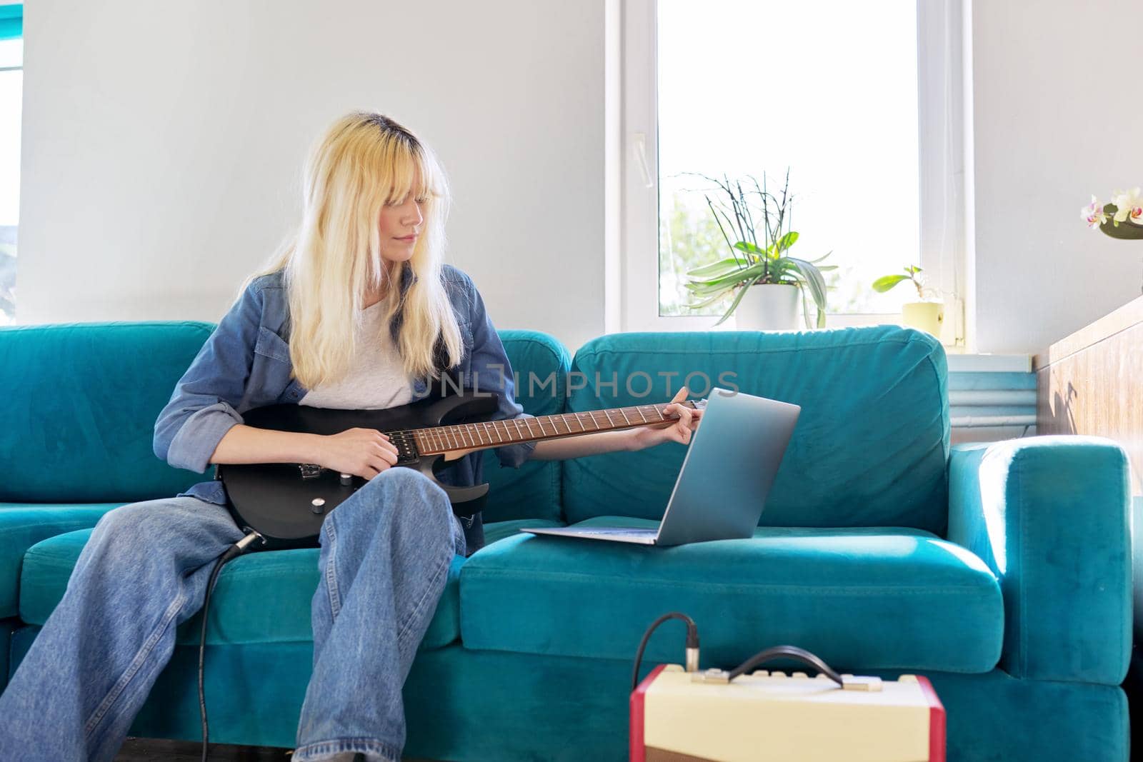 Hipster teenager girl playing electric guitar looking at laptop monitor by VH-studio