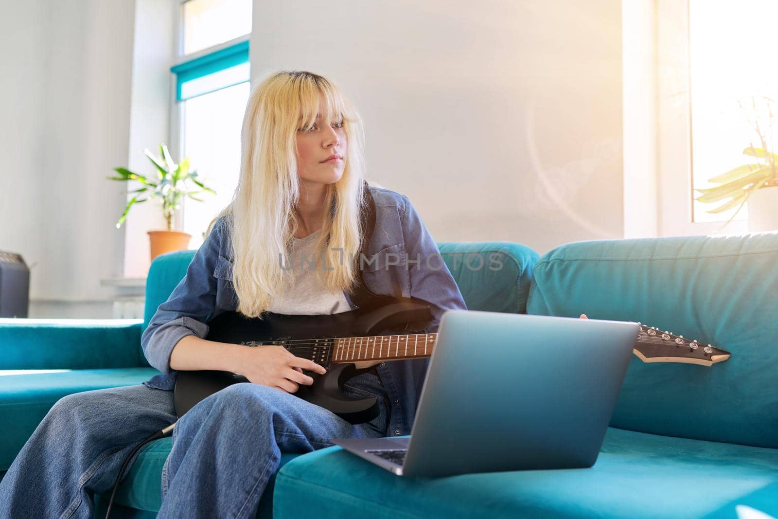 Hipster teenager girl playing electric guitar looking at laptop. Online learning music, songs, self-education, teen blogger musician recording video blog vlog, teaching, taking musical online courses