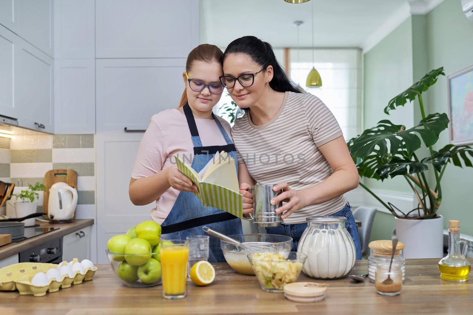 Mom and teenage daughter preparing apple pie in kitchen together by VH-studio