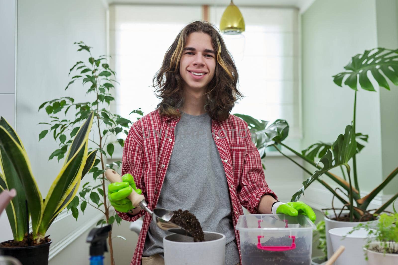 Guy teenager caring replanting indoor plants in pots by VH-studio