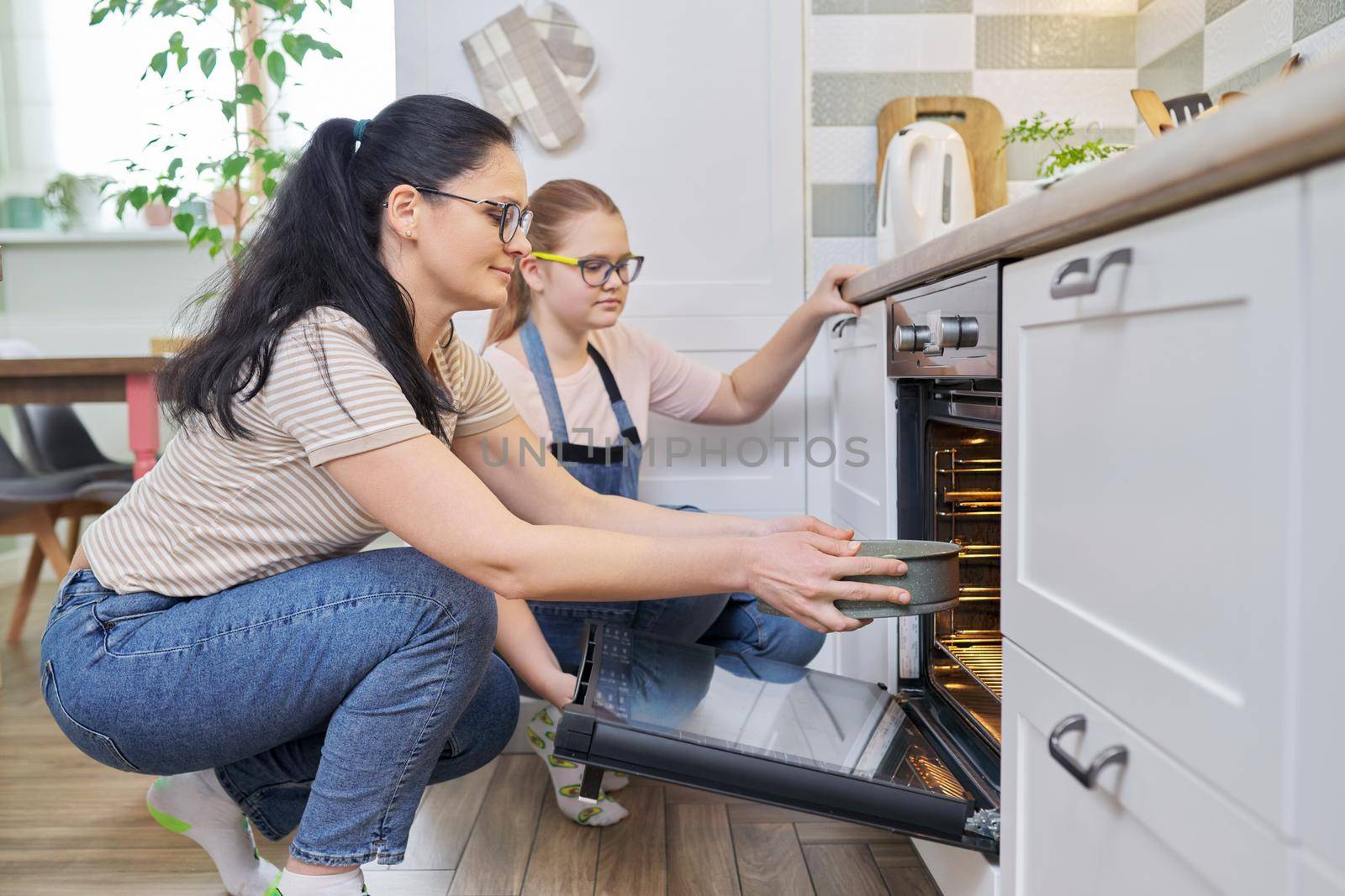 Mother and daughter preparing cake together, putting mold with dough in oven. Family, lifestyle, eating at home concept