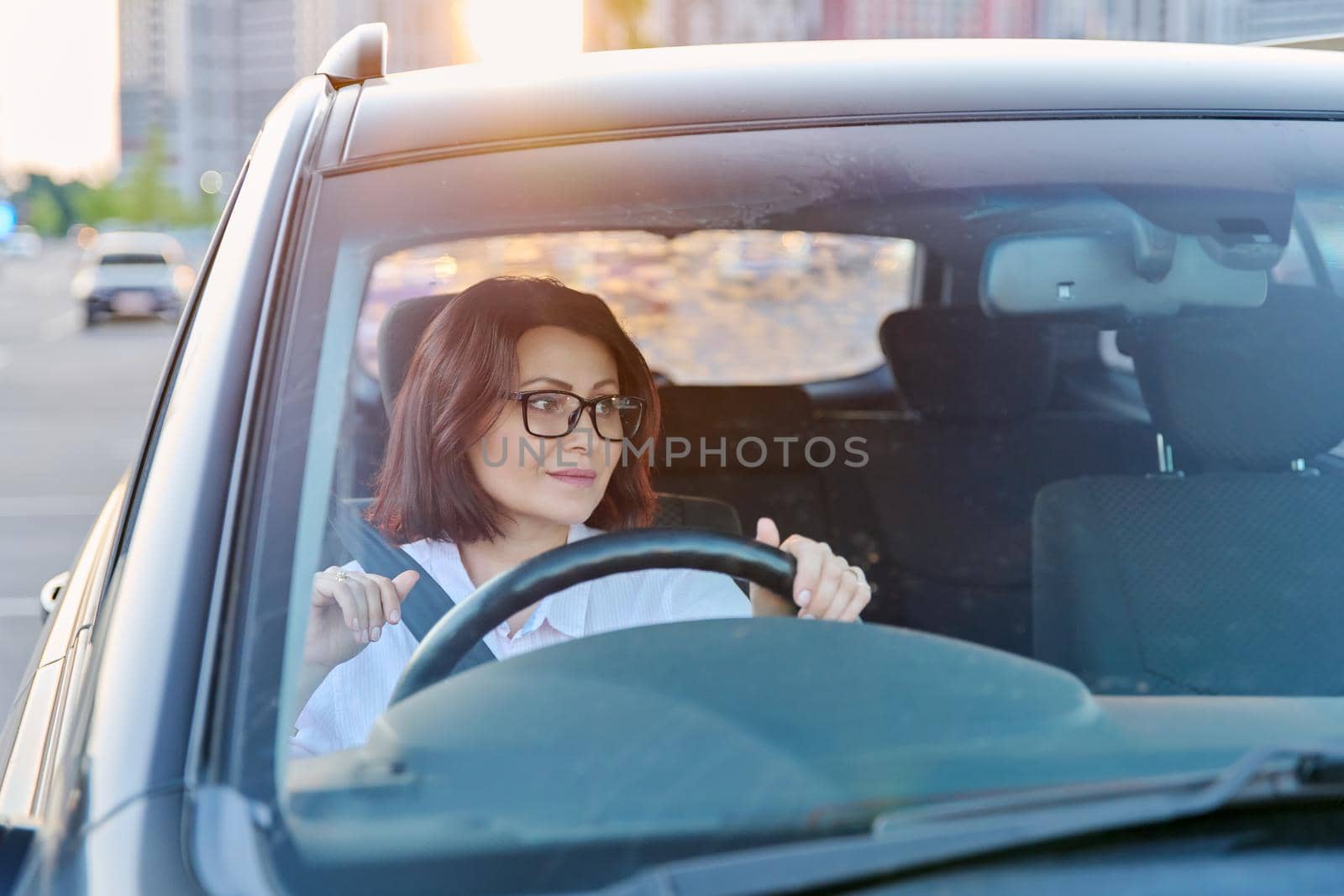 Middle-aged woman driver with glasses, female driving a car. Mature people, transportation, lifestyle concept