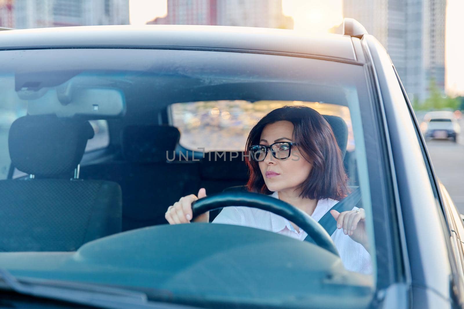 Middle-aged woman driver with glasses, female driving a car. Mature people, transportation, lifestyle concept