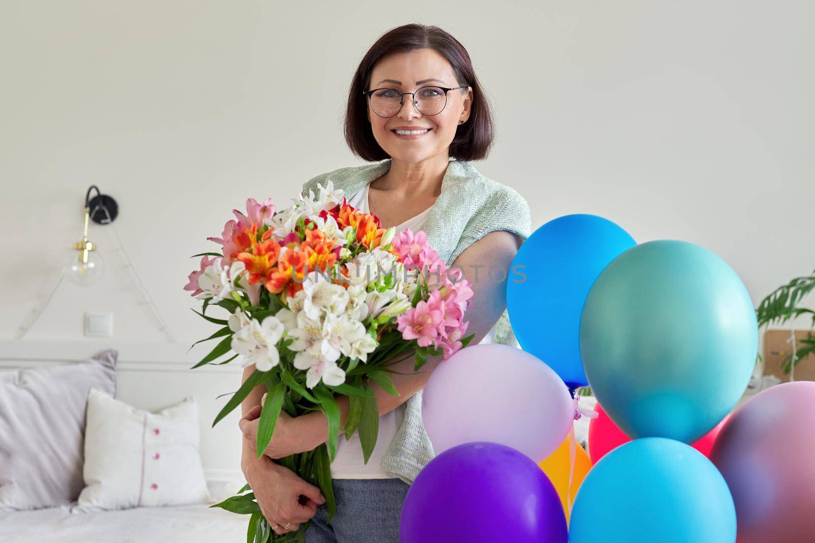 Birthday, 45 years old, happy middle-aged female with bouquet of flowers and balloons at home in the room. Mature age, celebration, anniversary, people concept