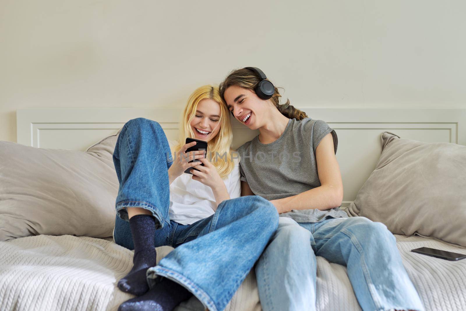 Happy laughing hipster teenagers male and female having fun using smartphone together by VH-studio
